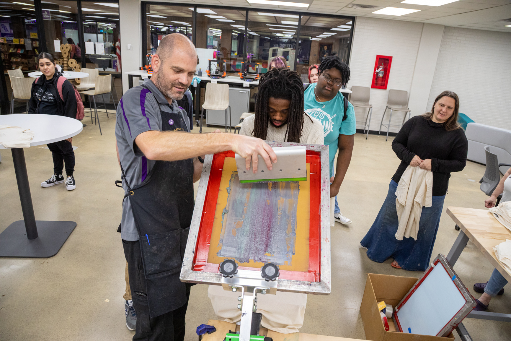 Professor Neal Cox demonstrates how to screen print on a T-shirt during a makerspace event inside the Ralph W. Steen Library.